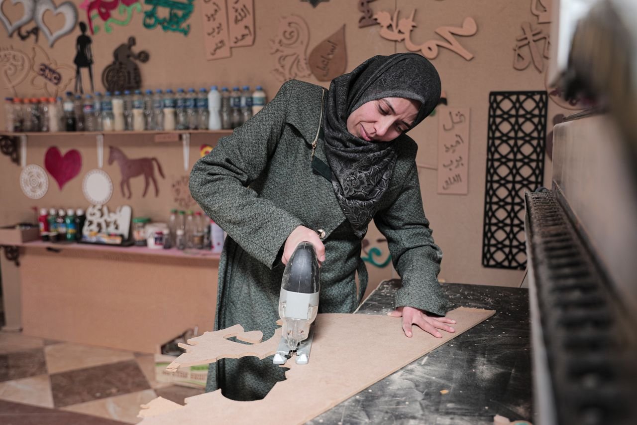 contact-img A Middle Eastern woman wearing a hijab skillfully works with wood in a creative Gaza workshop.