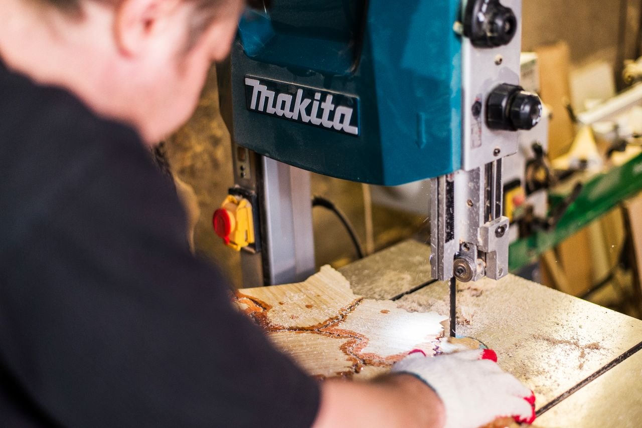 services-02 Close-up of a worker using a Makita band saw in a woodworking shop highlighting precision.